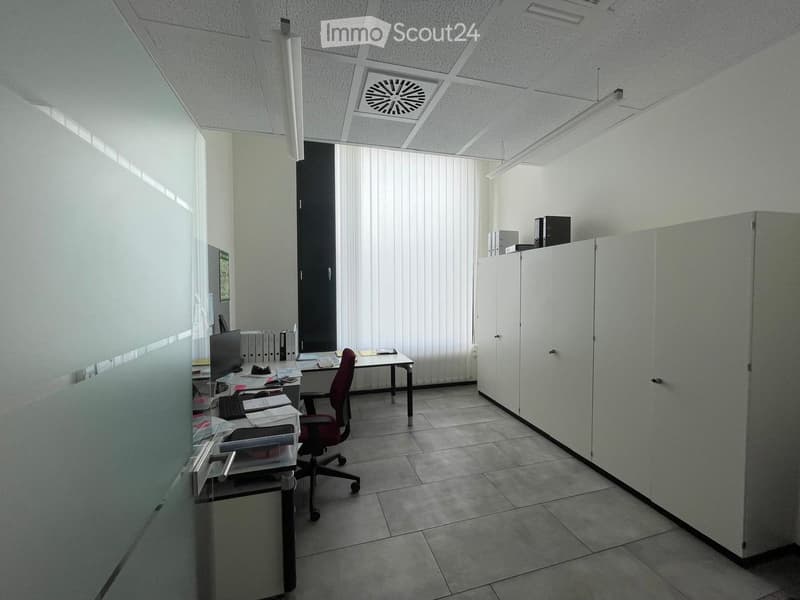 Office space with a chair, table, screen, keyboard, and cabinet. The room has tiled flooring and white walls.