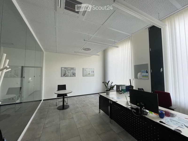 Modern office space with a desk, chair, screen, laptop, plant, and a small round table with a chair.