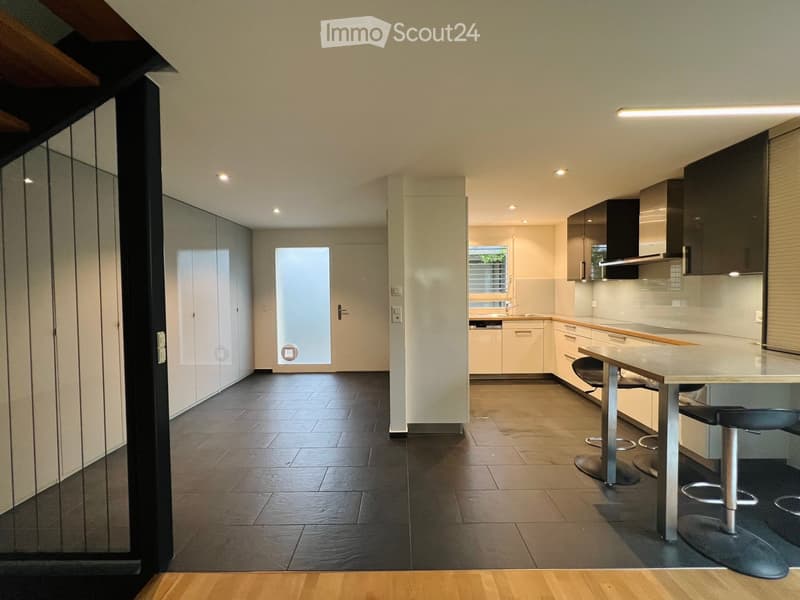Modern kitchen with white cabinets, a central island, and bar stools. Features a sleek design with integrated appliances and a large window.
