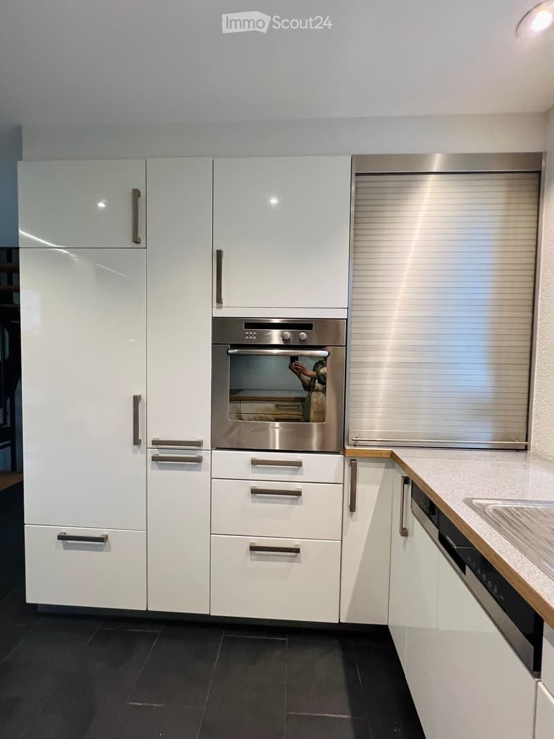 Modern kitchen with white cabinets, stainless steel appliances, and dark tiled flooring.