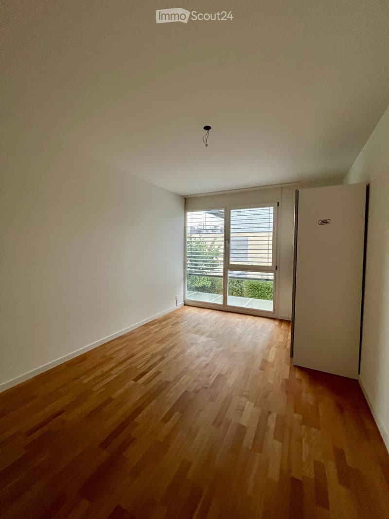 Empty room with wooden flooring, white walls, and a large sliding glass door leading to a balcony or outdoor area.