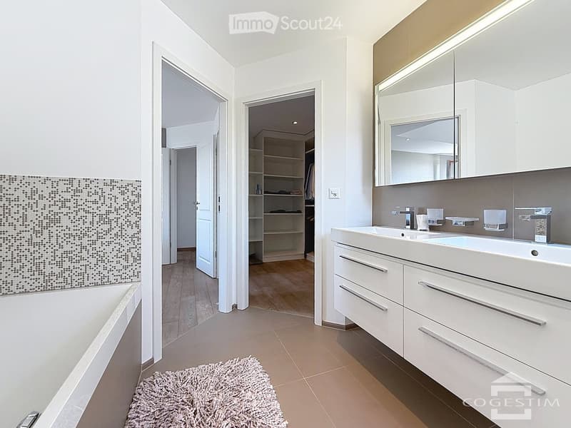 Bathroom. Modern bathroom with a white bathtub, double sink vanity with mirrored cabinet, and built-in shelving unit visible through an open doorway.