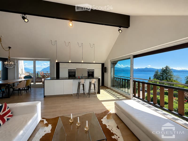 Open-plan living and dining area with a modern kitchen, large windows offering a scenic view, and contemporary furniture including a sofa, coffee table, and dining table.