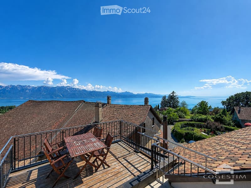 Wooden balcony with a table and chairs, overlooking a scenic view of mountains and a lake.