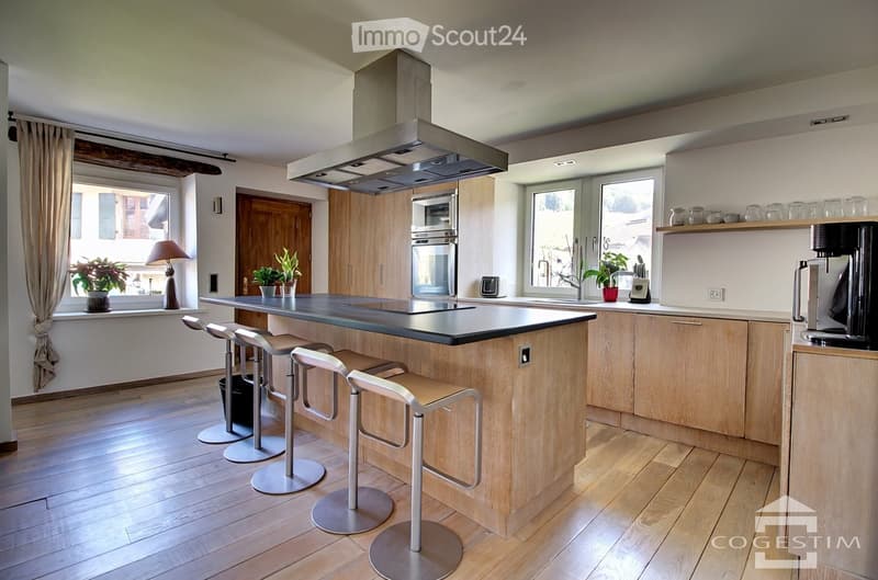 Modern kitchen with wooden cabinets, central island, four stools, stainless steel appliances, and large windows.