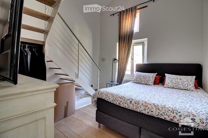 Cozy bedroom with a double bed, patterned bedding, nightstand, lamp, and a staircase leading to a loft area.