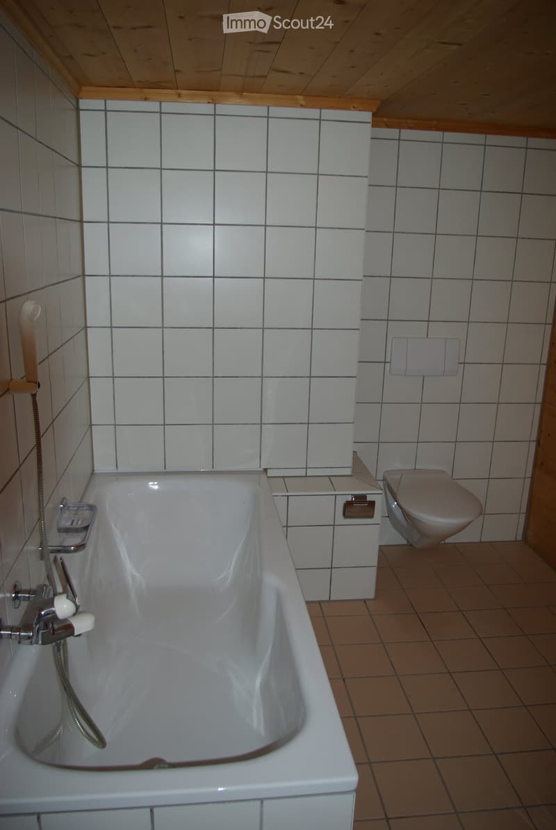 Bathroom with a white bathtub, toilet, tiled walls, and wooden ceiling.