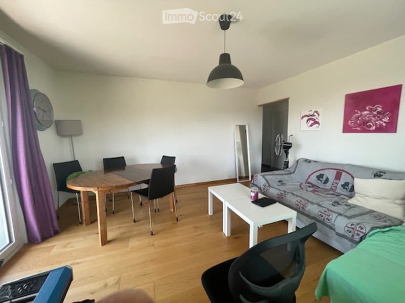 Bright, open-plan living and dining area with wooden flooring, white walls, and modern furniture including a sofa, coffee table, dining table, and chairs.