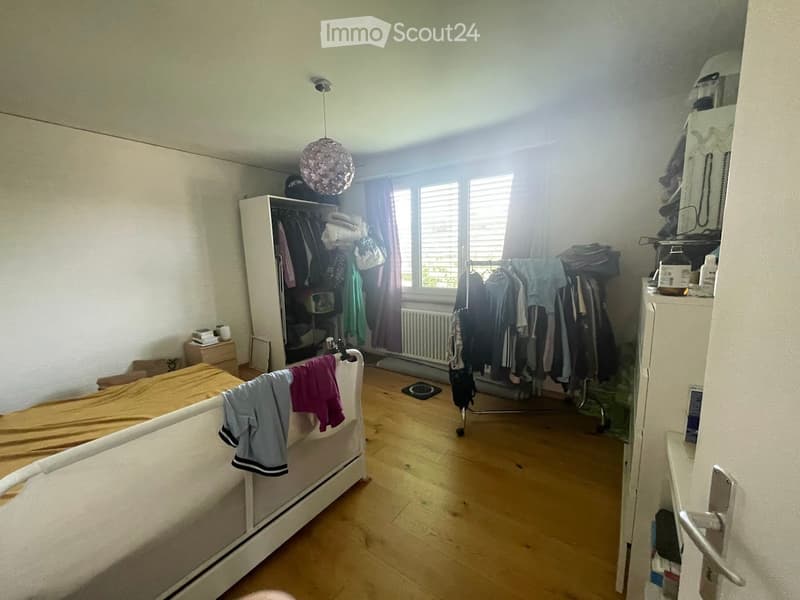 Bedroom with wooden flooring, a white bed with a yellow blanket, a wardrobe, a hanging clothes rack, and a decorative lamp.