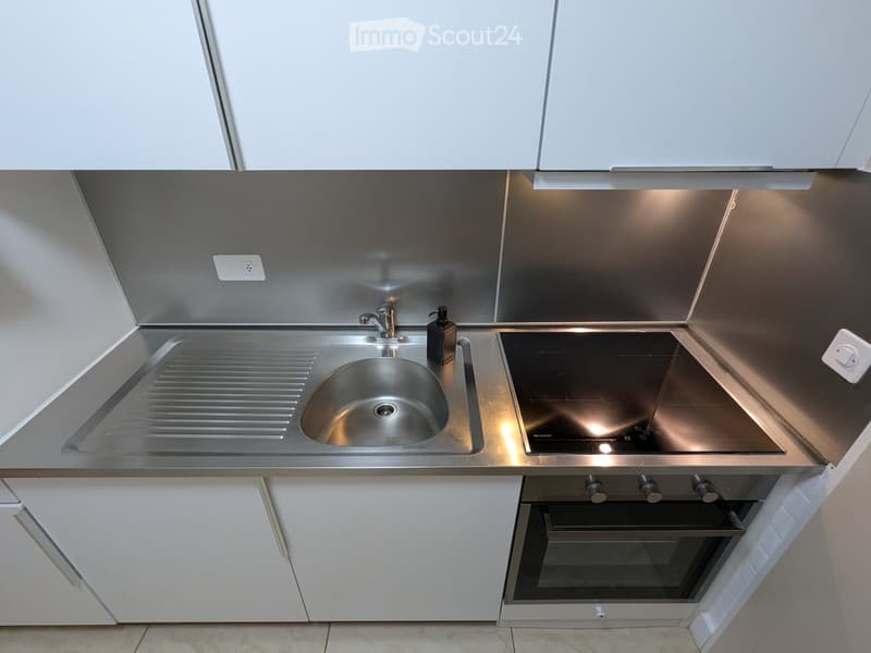 Modern kitchen with stainless steel sink, faucet, induction cooktop, oven, and white cabinets.
