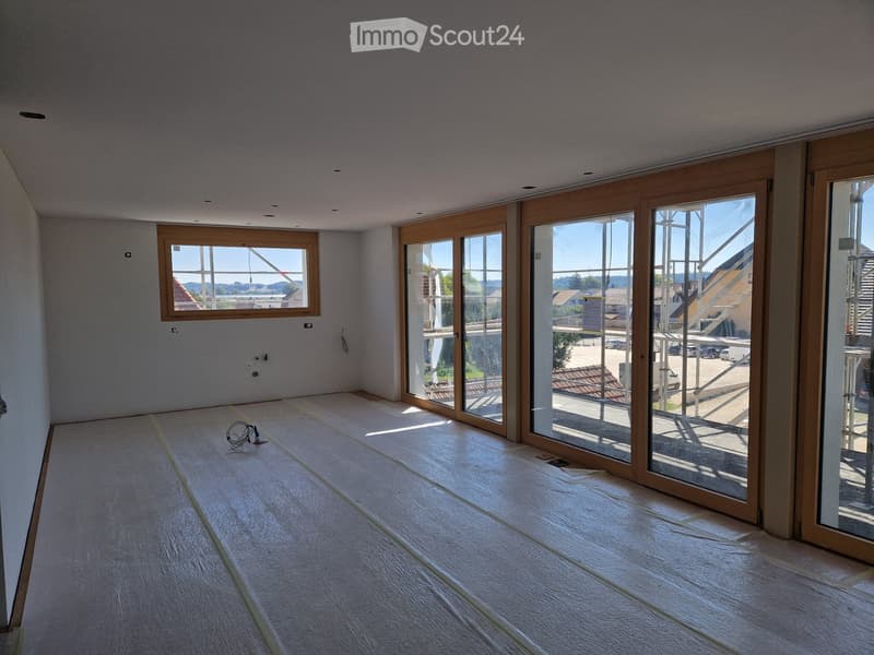 Empty room with light-colored walls, wooden flooring, and large glass sliding doors leading to a balcony or outdoor area. The room has a single window and visible electrical outlets.