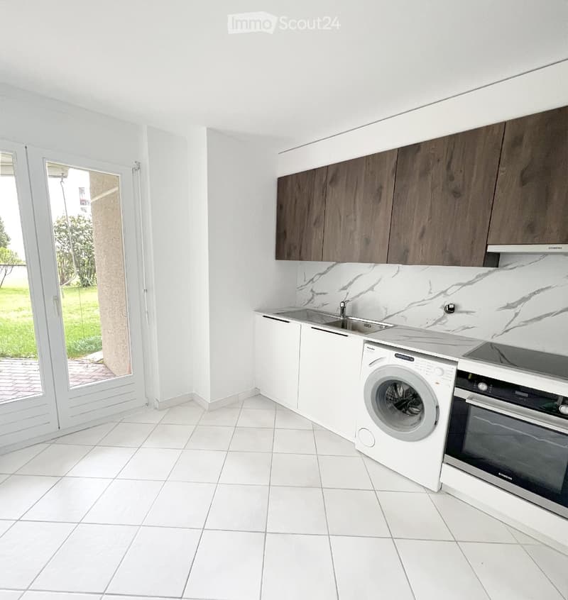 Modern kitchen with white tiled floors, white cabinets, and a marble backsplash. Features a sink, washing machine, and oven.