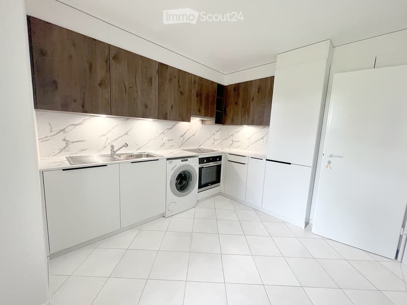 Modern kitchen with white tiled floor, white cabinets, marble backsplash, stainless steel sink, washing machine, and oven.