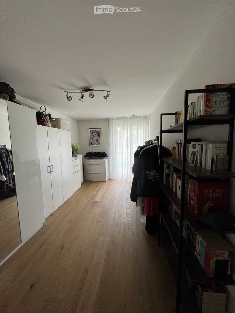 A well-lit hallway with wooden flooring, white walls, and modern furniture including a wardrobe, bookshelf, and a drawer unit.