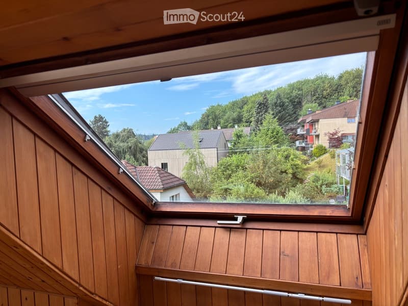 Wooden-framed window opening to a view of a suburban neighborhood with houses, trees, and a clear blue sky.