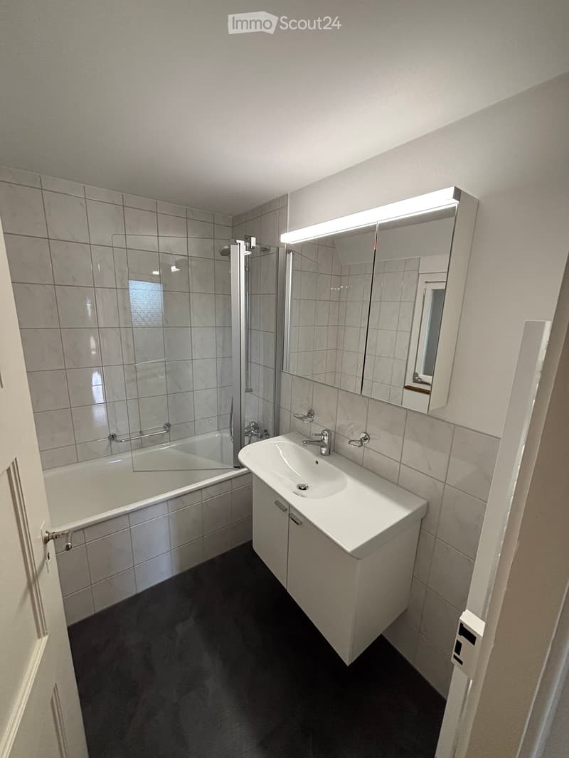 Modern bathroom with a white sink, mirror with built-in lighting, bathtub, and tiled walls.