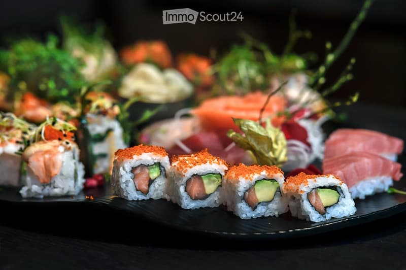 A plate of sushi rolls with avocado and salmon, garnished with orange sesame seeds and microgreens.