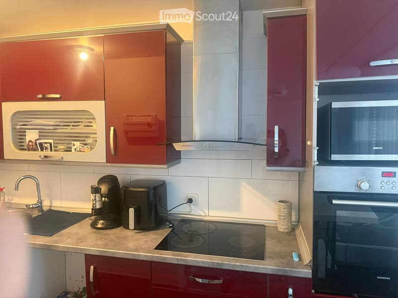 Modern kitchen with red cabinets, stainless steel appliances, induction stove, coffee maker, and microwave.