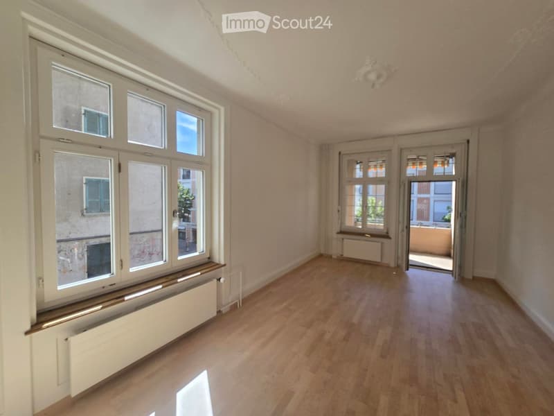 Empty room with wooden flooring, large windows, and a radiator. No furniture or equipment present.