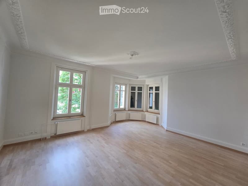 Empty room with wooden flooring, white walls, large windows, and radiators along the walls.