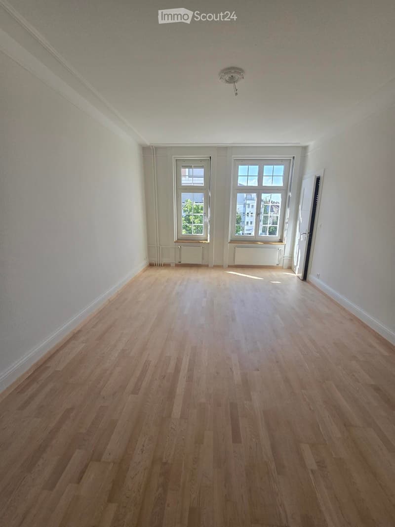 Empty room with wooden flooring, white walls, and two windows with white frames. A door is visible on the right side.