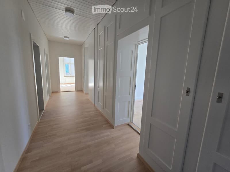 Empty hallway with wooden flooring, white walls, and several closed doors leading to other rooms.