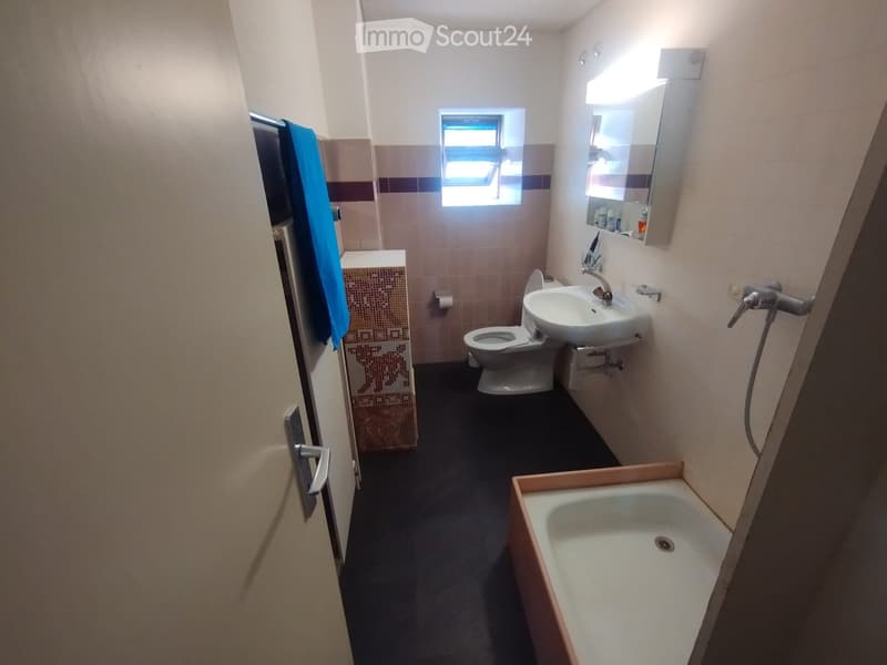Small bathroom with a toilet, sink, bathtub, and a mirror above the sink. The room has tiled walls and a window providing natural light.