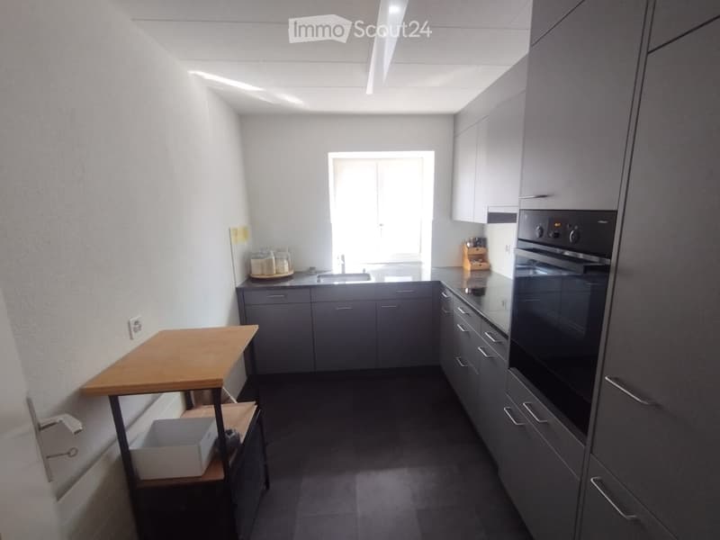 Modern kitchen with grey cabinets, a sink, an oven, and a wooden table with jars on the counter.