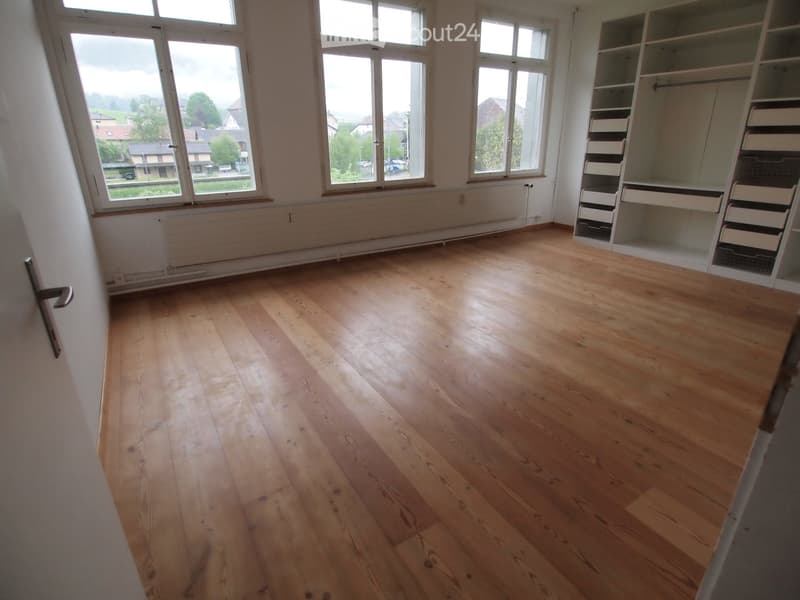 Empty room with wooden flooring, large windows, and built-in closet with drawers and shelves.