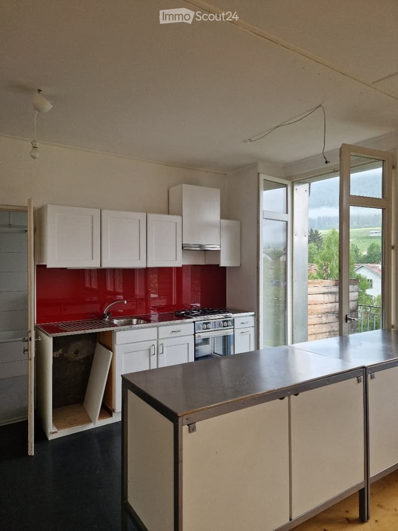 Modern kitchen with white cabinets, red backsplash, stainless steel appliances, and a central island.