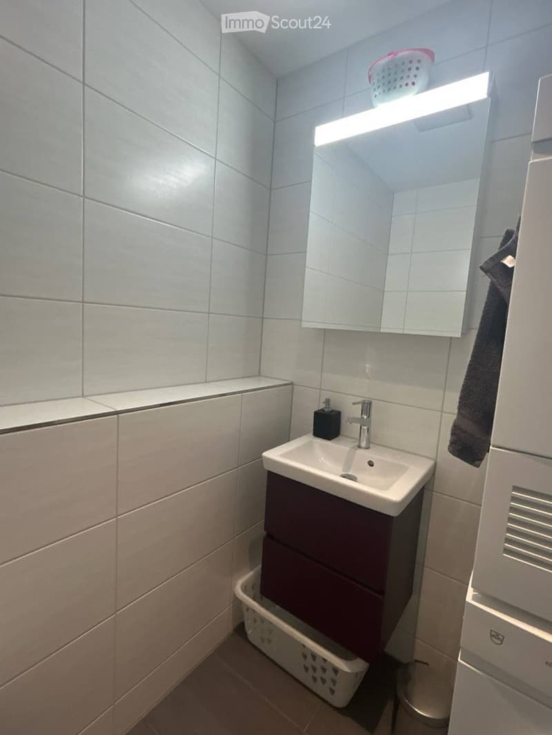 Modern bathroom with a white sink, dark wooden cabinet, mirror with built-in lighting, and a laundry basket on the floor.