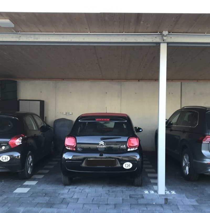 Garage with three parked cars under a covered structure, concrete walls, and tiled floor.