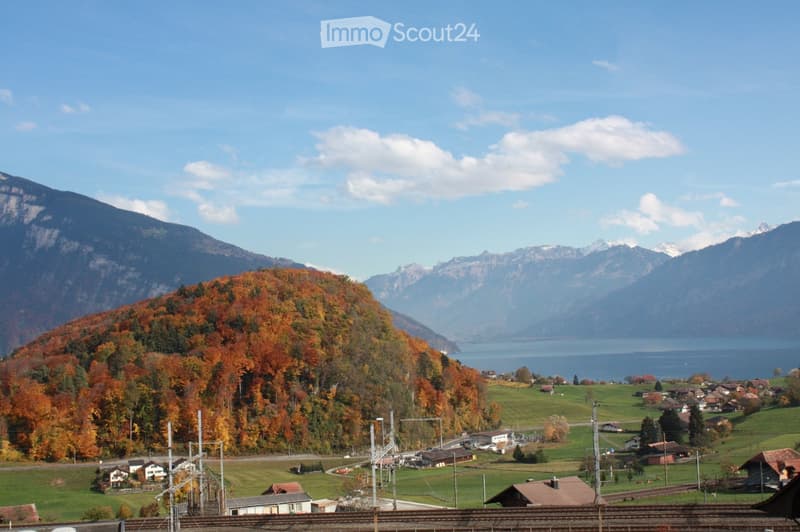 Scenic view of a village nestled in a valley surrounded by autumn-colored trees and mountains, with a lake in the background.