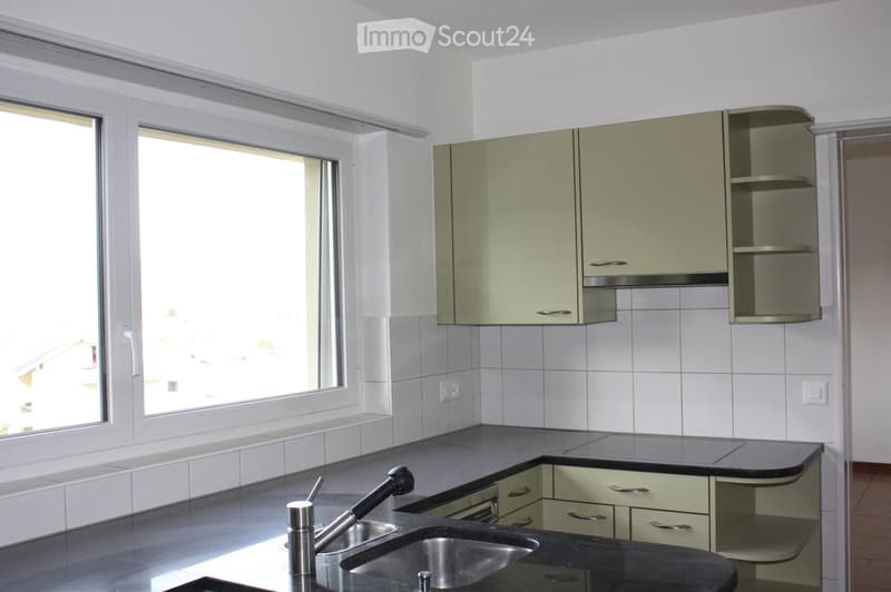 Modern kitchen with light green cabinets, black countertops, stainless steel sink, and large windows providing natural light.