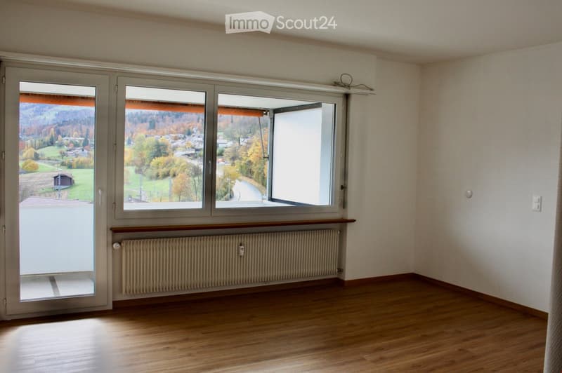 Empty room with wooden flooring, large windows, radiator, and a view of a rural landscape.