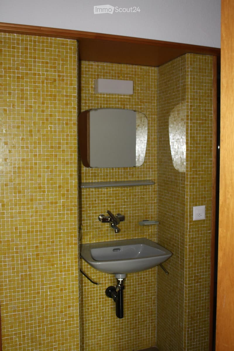 Small bathroom with yellow tiled walls, a sink with a faucet, a toilet, and a shelf above the sink.