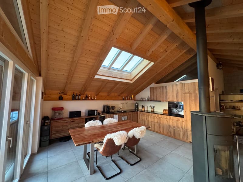 Bright kitchen with wooden cabinets, a dining table with four chairs, and modern appliances including an oven, microwave, and coffee maker. The room features exposed wooden beams and skylights.