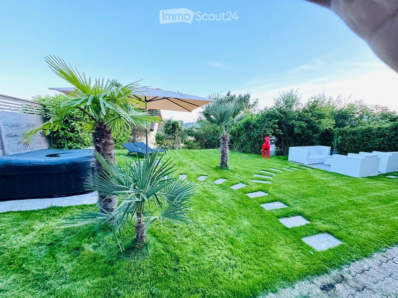 Well-maintained garden with a hot tub, lounge chairs, a large umbrella, and modern seating area.