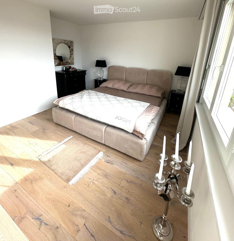 Cozy bedroom with a light-colored sofa, wooden floor, nightstands, lamps, and a decorative candle holder.