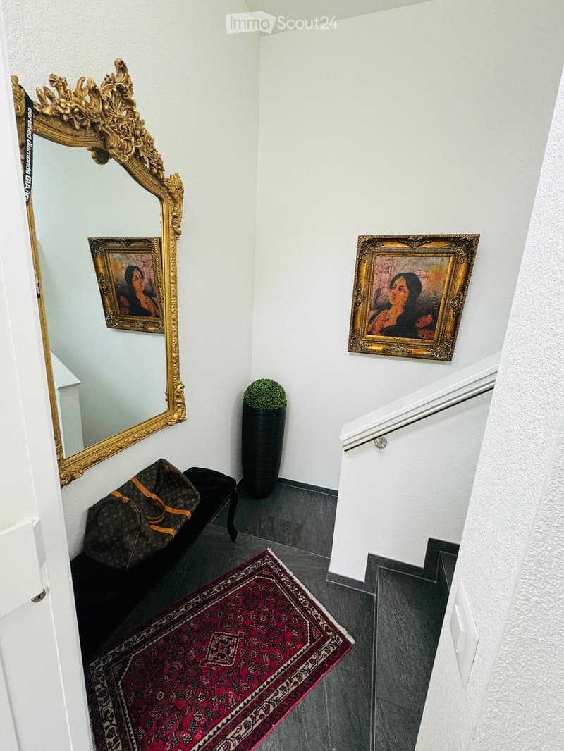 Staircase with ornate mirror, framed paintings, potted plant, and a small bench with a bag on it.