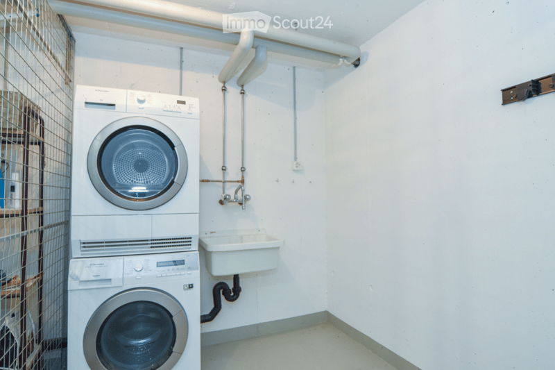 Compact bathroom with stacked washing machine and dryer, a small sink, and white tiled walls.