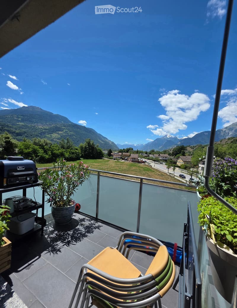 Balcony with a scenic mountain view, featuring a stack of chairs, a small table, potted plants, and a grill.