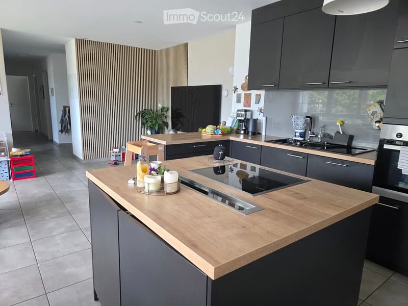 Modern kitchen with grey cabinets, wooden countertops, induction cooktop, sink, and various appliances. Includes a candle holder and a small plant on the counter.
