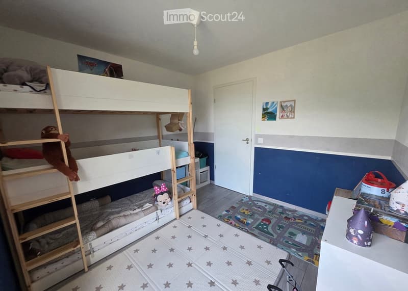 A cozy children's bedroom with a white bunk bed, colorful toys, a play mat, and a small table with a stool.
