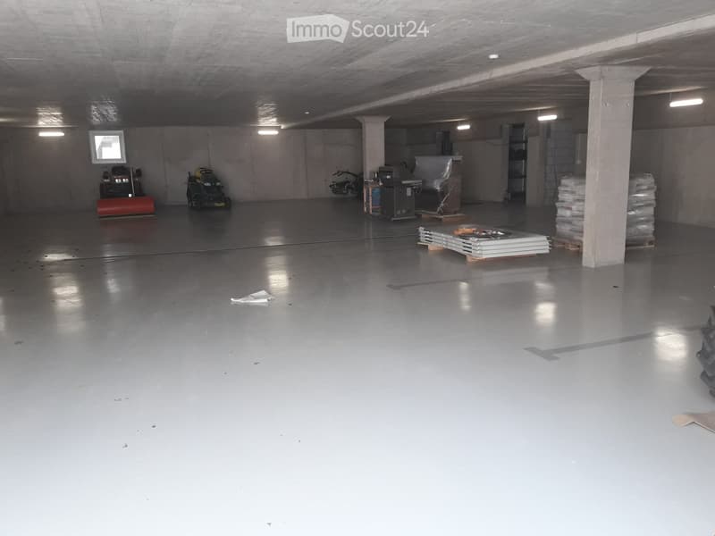 Concrete floors, ceiling and walls, lights installed on the ceiling, machinery equipment placed, storage boxes stacked, open space.