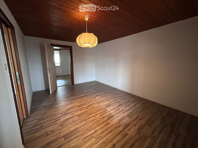 Empty hallway with wooden flooring, white walls, and a hanging light fixture. Open doors lead to adjacent rooms.