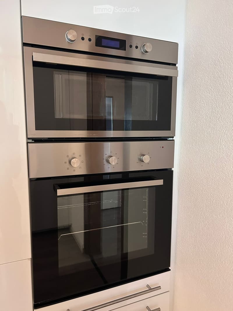 Modern stainless steel double oven with digital controls and glass doors, mounted on white cabinetry.