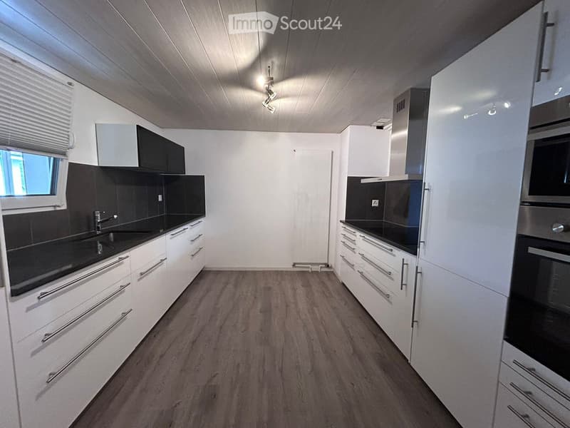 Modern kitchen with white cabinets, black countertops, and wooden flooring. Features a sink, faucet, and built-in oven.