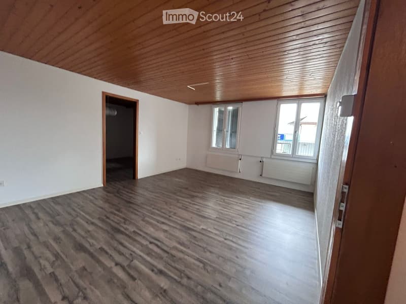 Empty room with wooden flooring, white walls, and a wooden ceiling. Features a door leading to another room and windows with blinds.