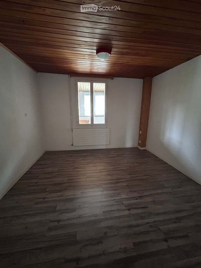 Empty room with wooden flooring, white walls, and a wooden ceiling. Features a window with a radiator below it and a single ceiling light fixture.
